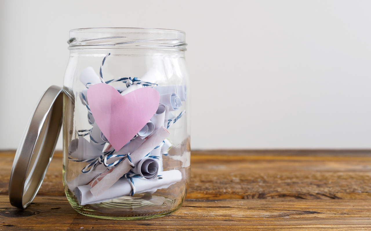 Einmachglas mit rosa Herz und zusammengerollten Notizzetteln, weißer Hintergrund