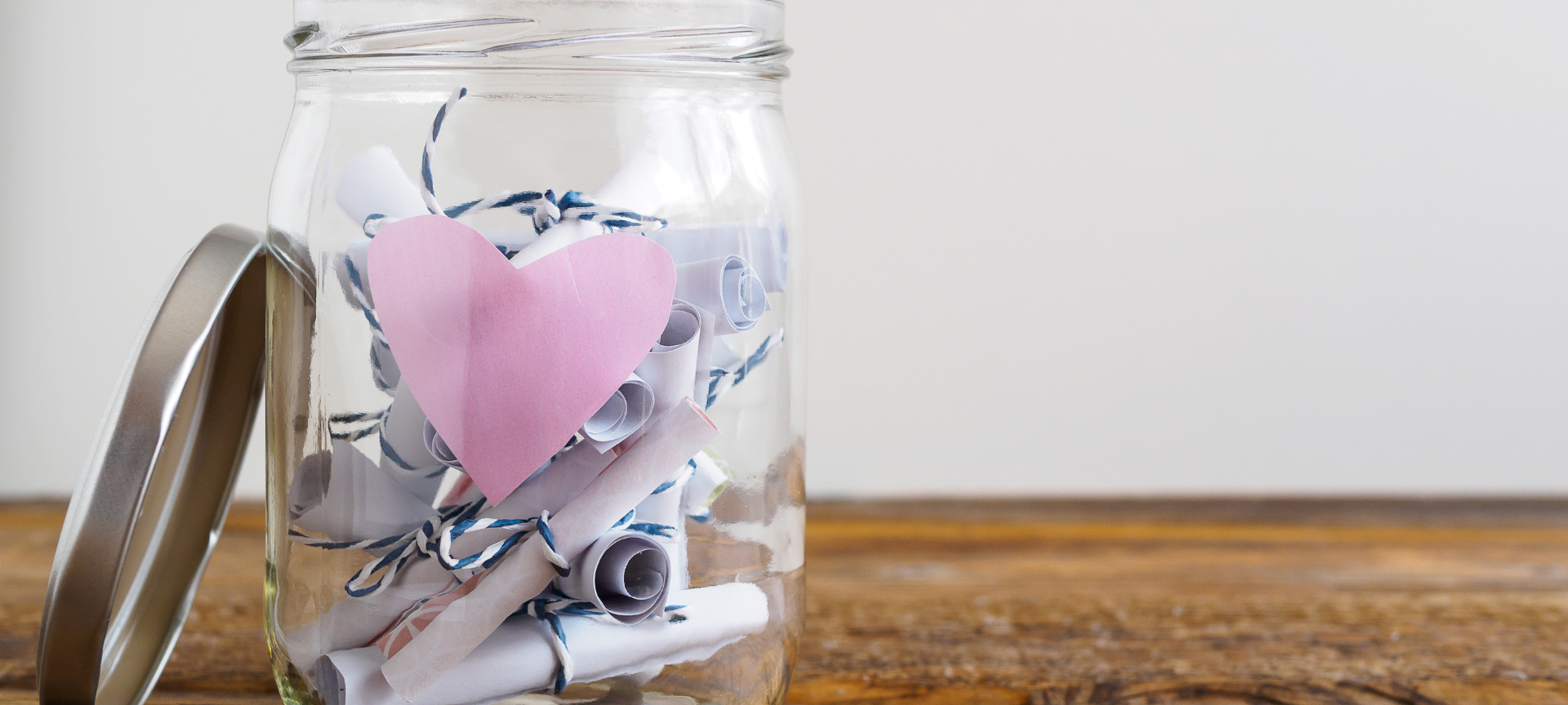 Einmachglas mit rosa Herz und zusammengerollten Notizzetteln, weißer Hintergrund